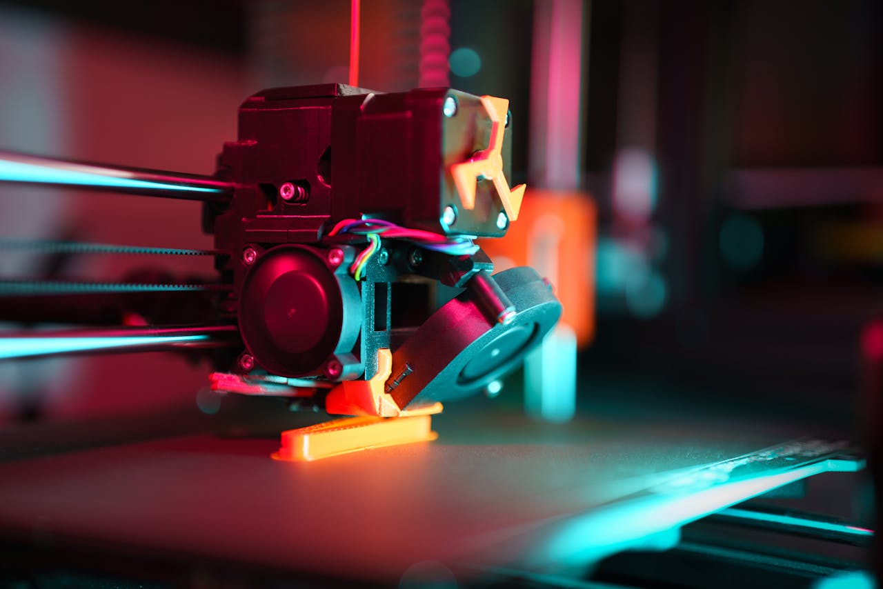 gallery-03 Close-up of a 3D printer in action with neon lighting, showcasing technology in prototyping.